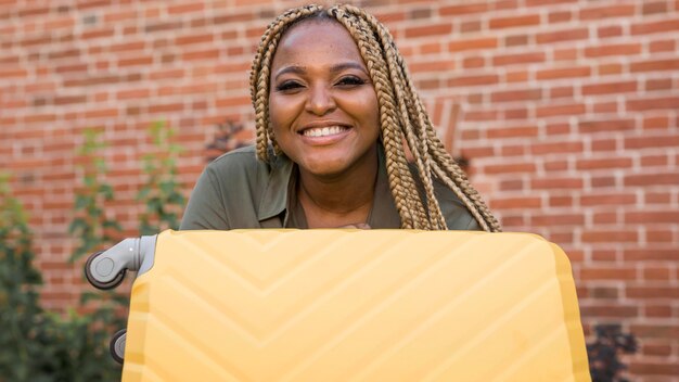 Mujer sonriente sosteniendo su equipaje amarillo