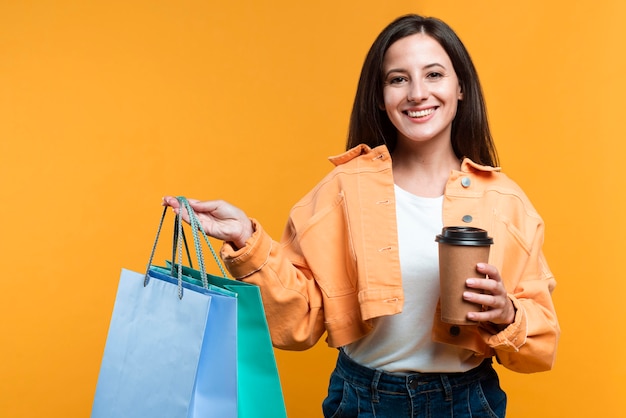 Mujer sonriente sosteniendo una taza de café y bolsas de la compra.