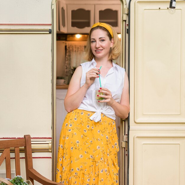 Mujer sonriente sosteniendo un vaso de limonada junto a una caravana