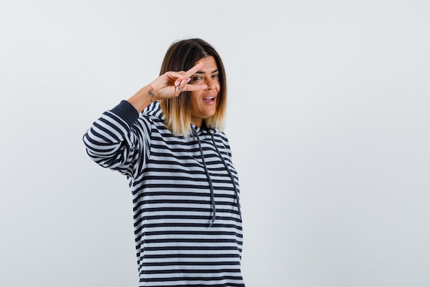 La mujer sonriente sostiene los dedos cerca del ojo en el fondo blanco