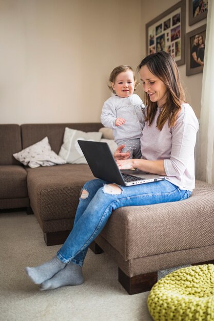 Mujer sonriente con su hija trabajando en la computadora portátil