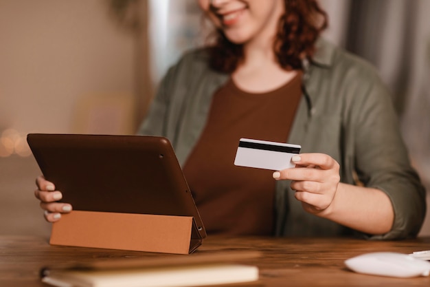 Mujer sonriente con su tableta en casa con tarjeta de crédito