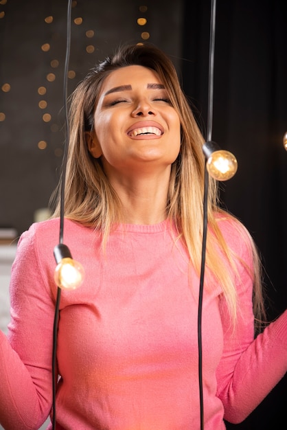 Una mujer sonriente en suéter posando junto a lámparas de luz.