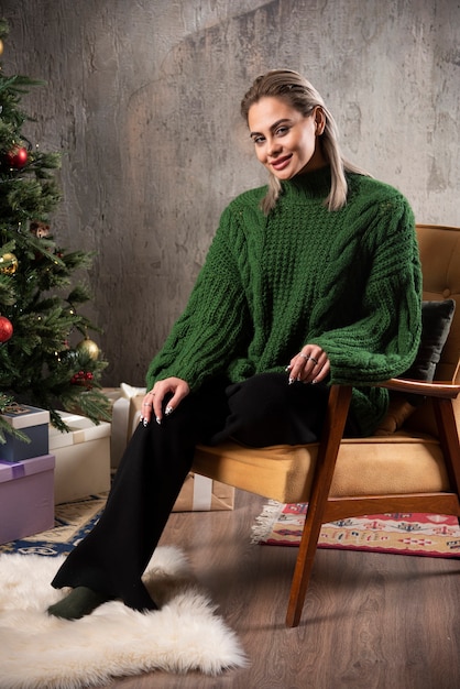 Mujer sonriente en suéter verde cálido sentado en la silla y posando
