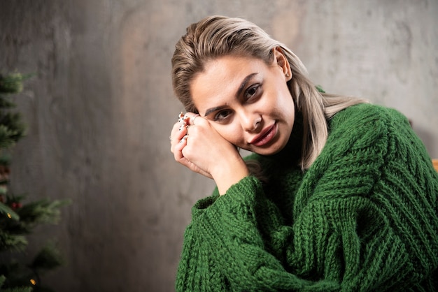 Mujer sonriente en suéter verde cálido sentado en la silla y posando