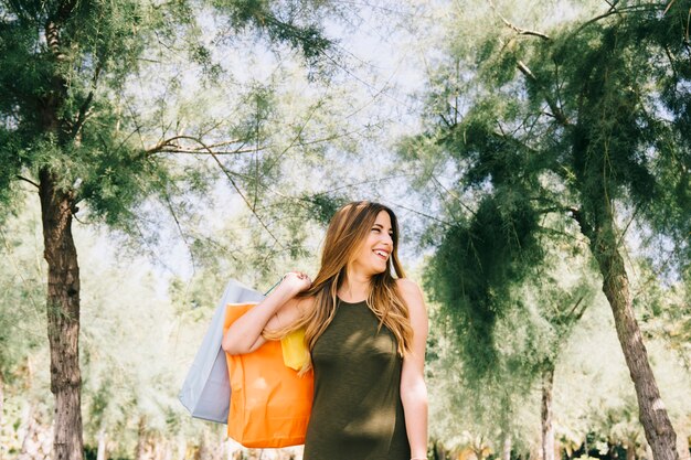 Mujer sonriente sujetando bolsas de compras en la naturaleza