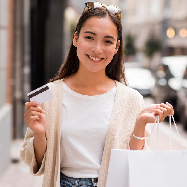 Mujer sonriente con tarjeta de crédito y bolsas de compras al aire libre