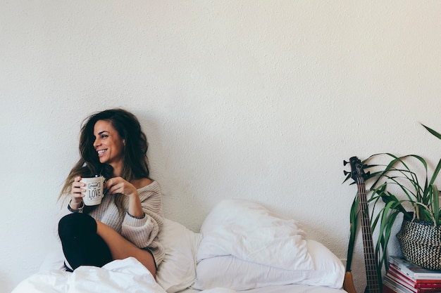 Mujer sonriente con taza en la cama