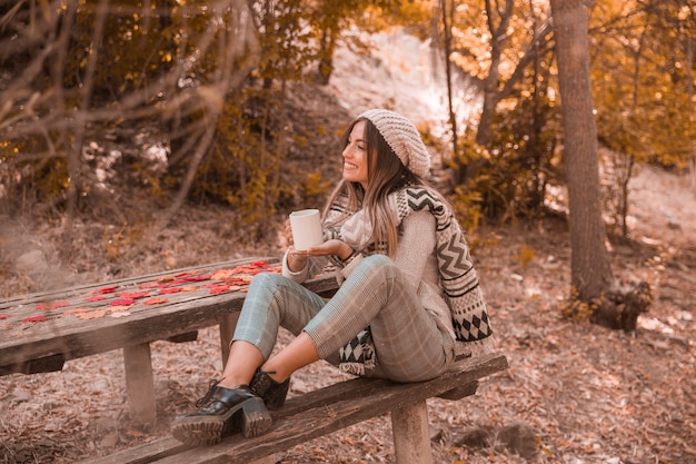 Mujer sonriente con taza cerca de la mesa en el parque