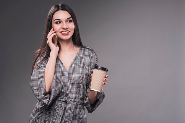 Mujer sonriente con taza hablando en teléfono inteligente