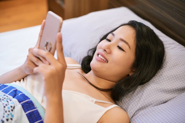 Mujer sonriente con teléfono abrazando en la cama