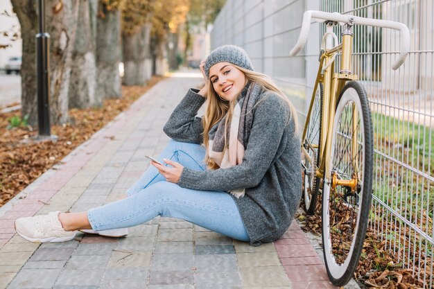 Mujer sonriente con teléfono inteligente cerca de bicicleta