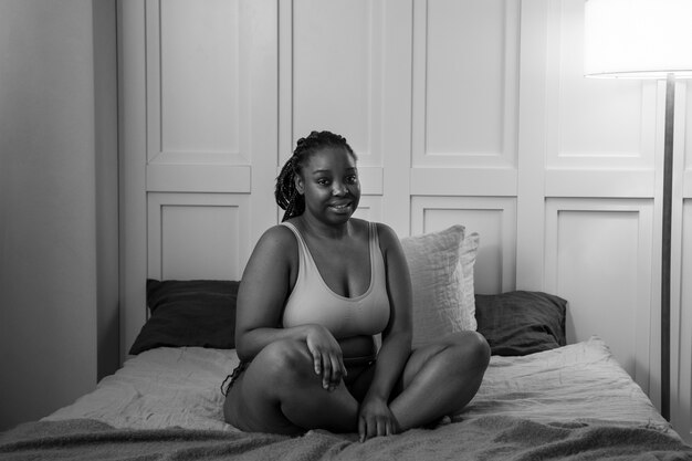 Mujer sonriente de tiro completo en la cama en blanco y negro