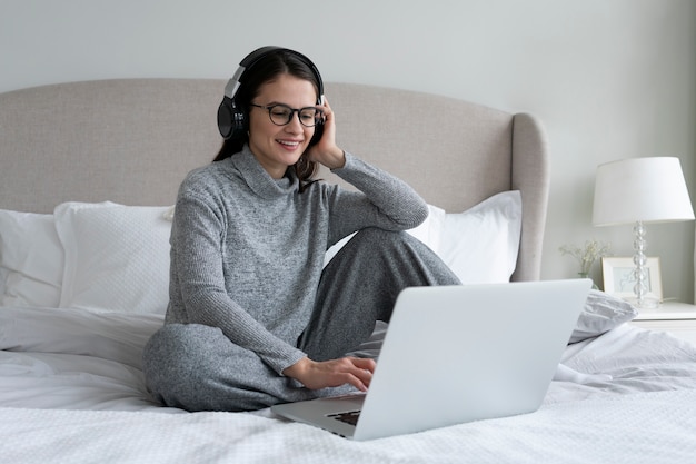 Mujer sonriente de tiro completo con computadora portátil en el dormitorio