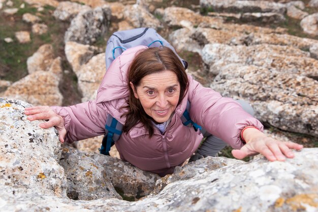 Mujer sonriente de tiro completo escalando roca