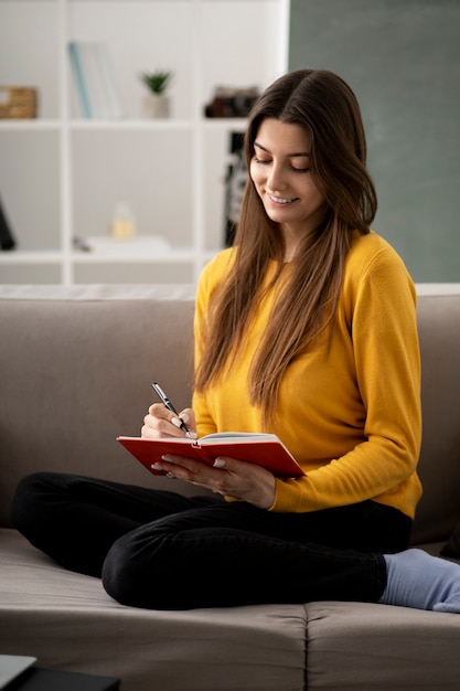 Mujer sonriente de tiro completo escribiendo en el cuaderno