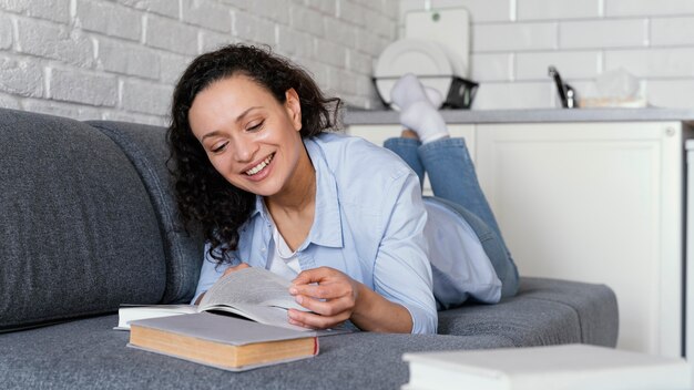 Mujer sonriente de tiro completo leyendo en el sofá