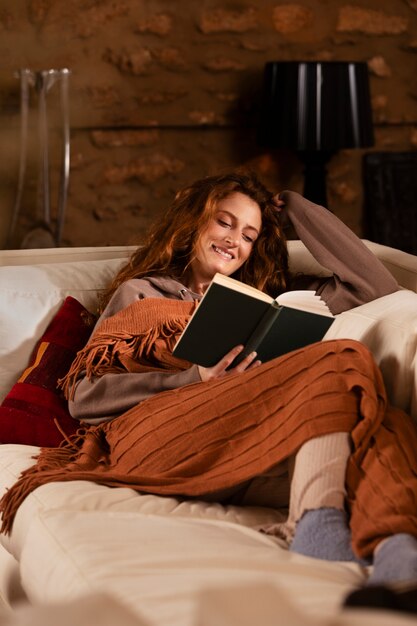 Mujer sonriente de tiro completo leyendo en el sofá