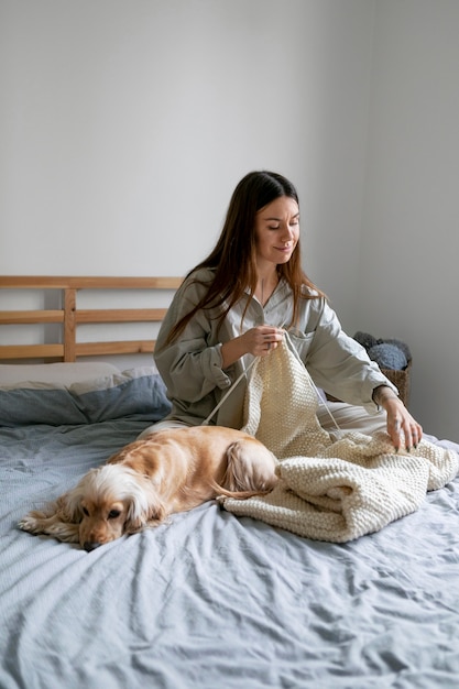 Mujer sonriente de tiro completo con lindo perro tejiendo