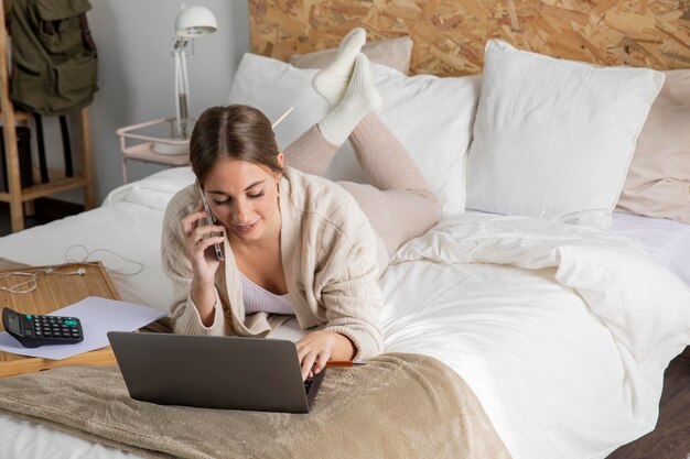 Mujer sonriente de tiro completo que trabaja en la cama