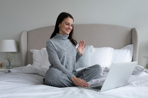 Mujer sonriente de tiro completo sentada en la cama