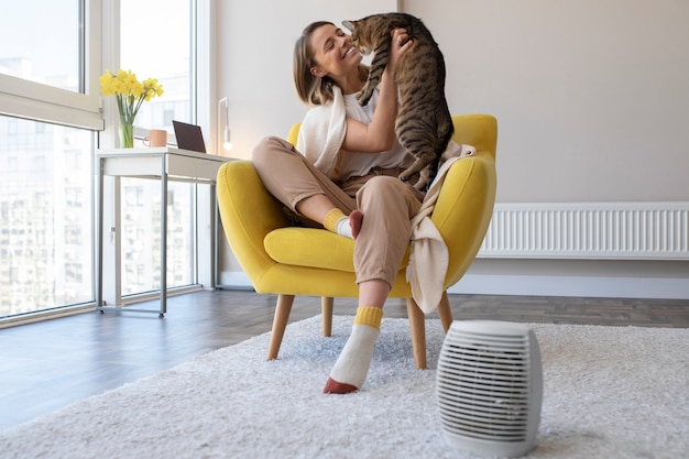 Mujer sonriente de tiro completo sentada en una silla con gato