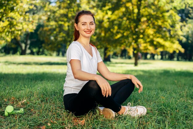 Mujer sonriente de tiro completo sentada sobre el césped