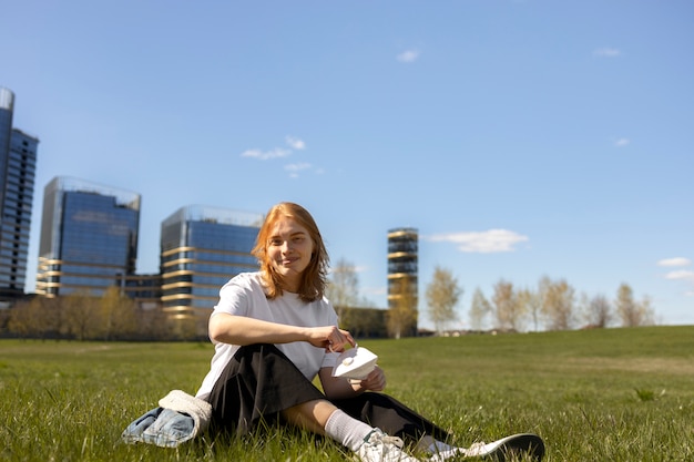 Foto gratuita mujer sonriente de tiro completo sentada sobre el césped