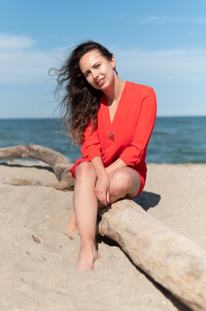 Mujer sonriente de tiro completo sentado en la playa