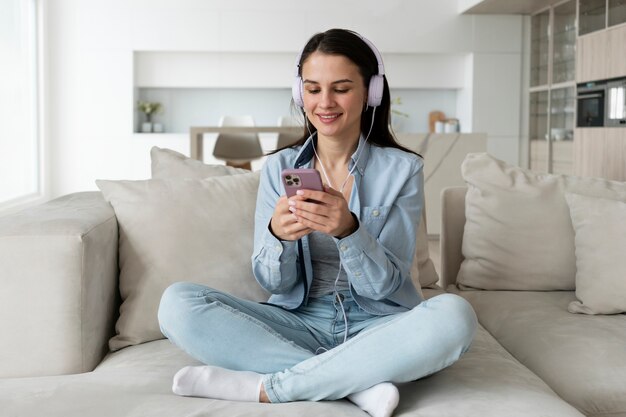 Mujer sonriente de tiro completo en el sofá con teléfono inteligente