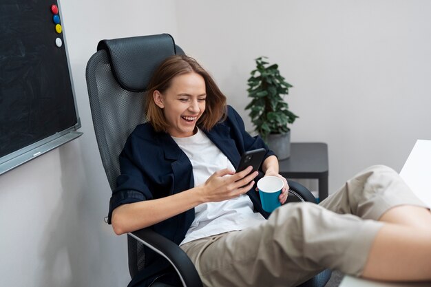 Mujer sonriente de tiro completo sosteniendo el teléfono en el trabajo