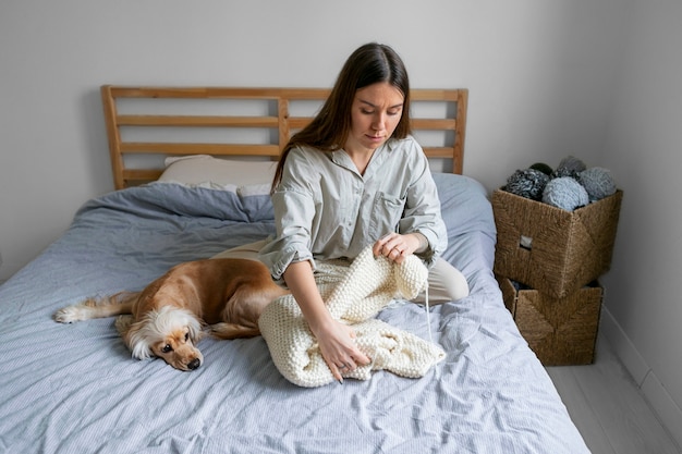 Mujer sonriente de tiro completo tejiendo en casa