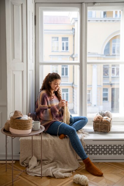 Mujer sonriente de tiro completo tejiendo en casa