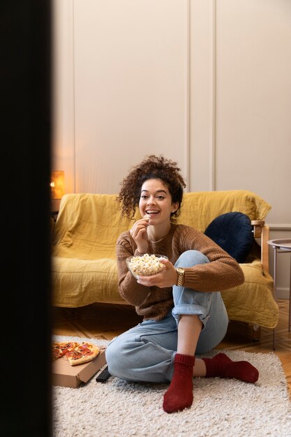 Mujer sonriente de tiro completo viendo la televisión