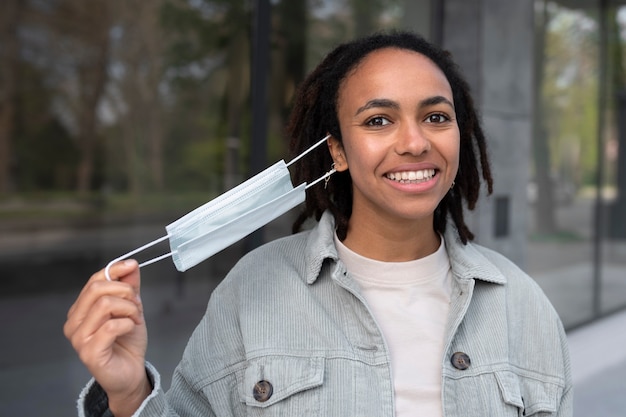 Mujer sonriente de tiro medio quitándose la máscara afuera