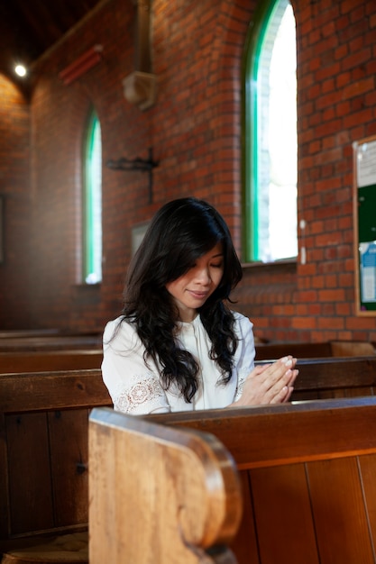 Mujer sonriente de tiro medio rezando en la iglesia