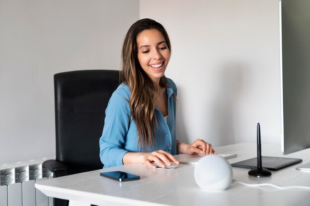 Mujer sonriente de tiro medio sentada en el escritorio