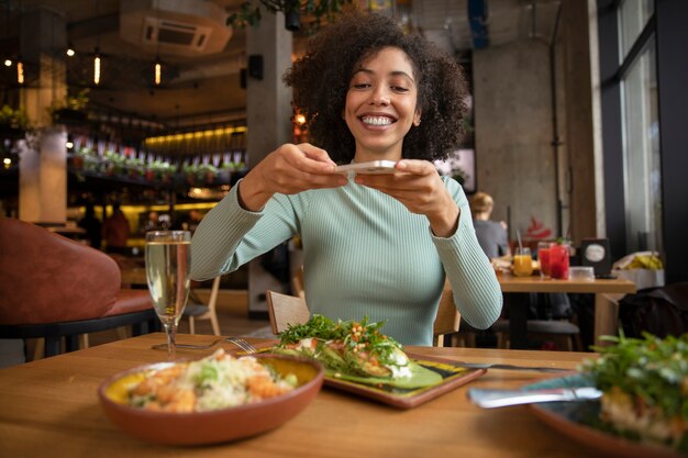 Mujer sonriente de tiro medio tomando fotos de comida