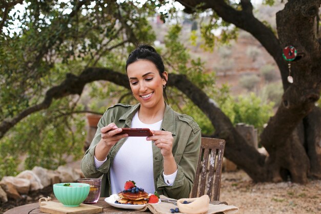 Mujer sonriente de tiro medio tomando fotos de comida