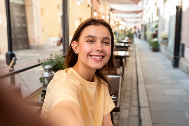 Mujer sonriente de tiro medio tomando selfie afuera