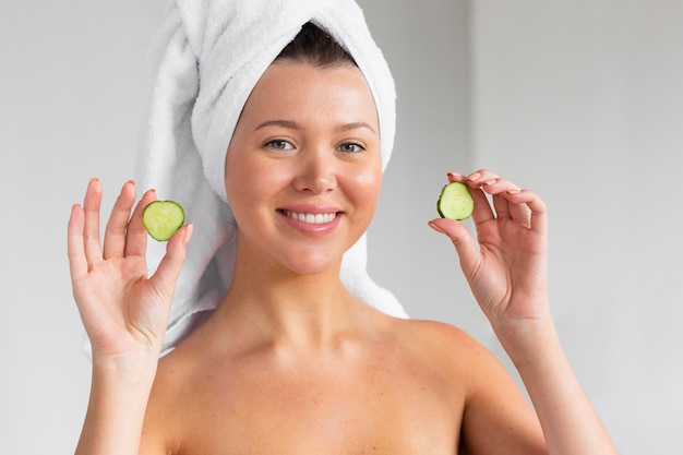 Mujer sonriente con toalla en la cabeza con rodajas de pepino