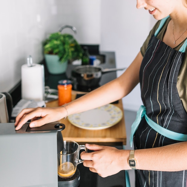 Mujer sonriente tomando café de cafetera en la cocina