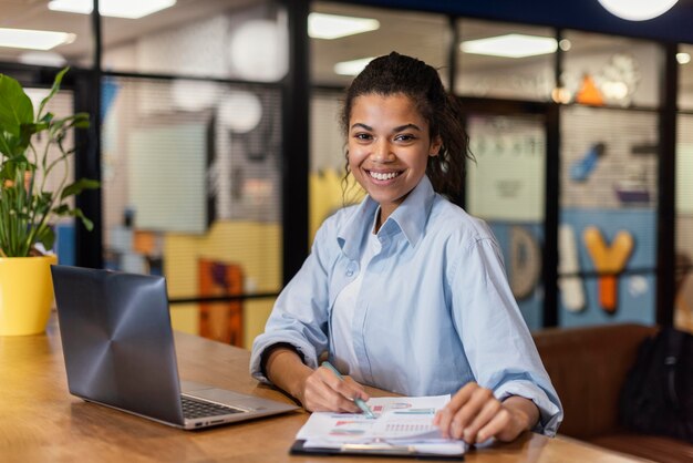 Mujer sonriente trabajando con ordenador portátil y papeles en la oficina