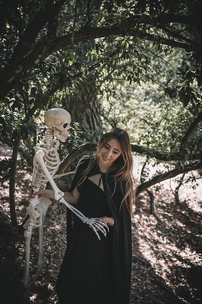 Mujer sonriente en traje de bruja sosteniendo por encima de la cabeza esqueleto