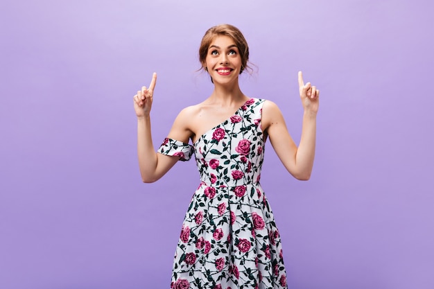 Mujer sonriente en traje floral apunta al lugar para el texto. Chica con estilo alegre en ropa brillante moderna posando sobre fondo aislado.