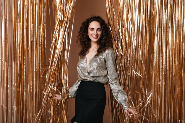 Mujer sonriente en traje plateado posa felizmente sobre fondo dorado