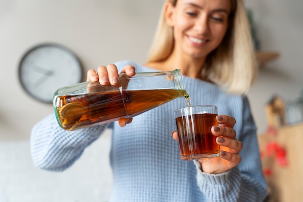 Mujer sonriente vertiendo kombucha ángulo bajo