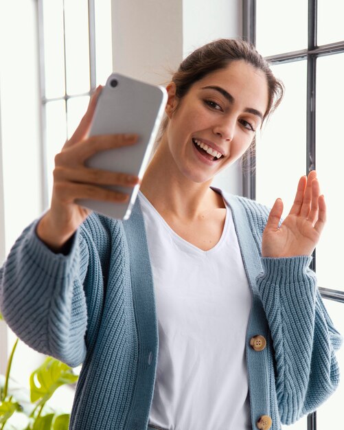 Mujer sonriente videollamada a alguien con smartphone en casa