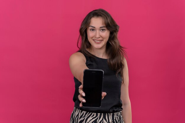 Mujer sonriente vistiendo camiseta negra sostuvo el teléfono en la pared rosa