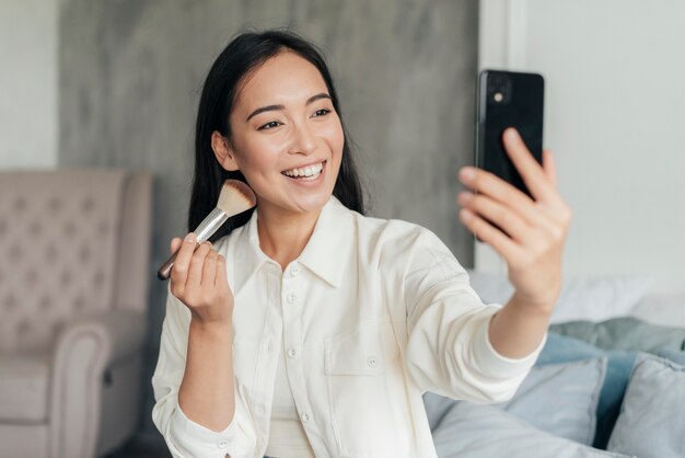 Mujer sonriente vlogueando con un pincel de maquillaje